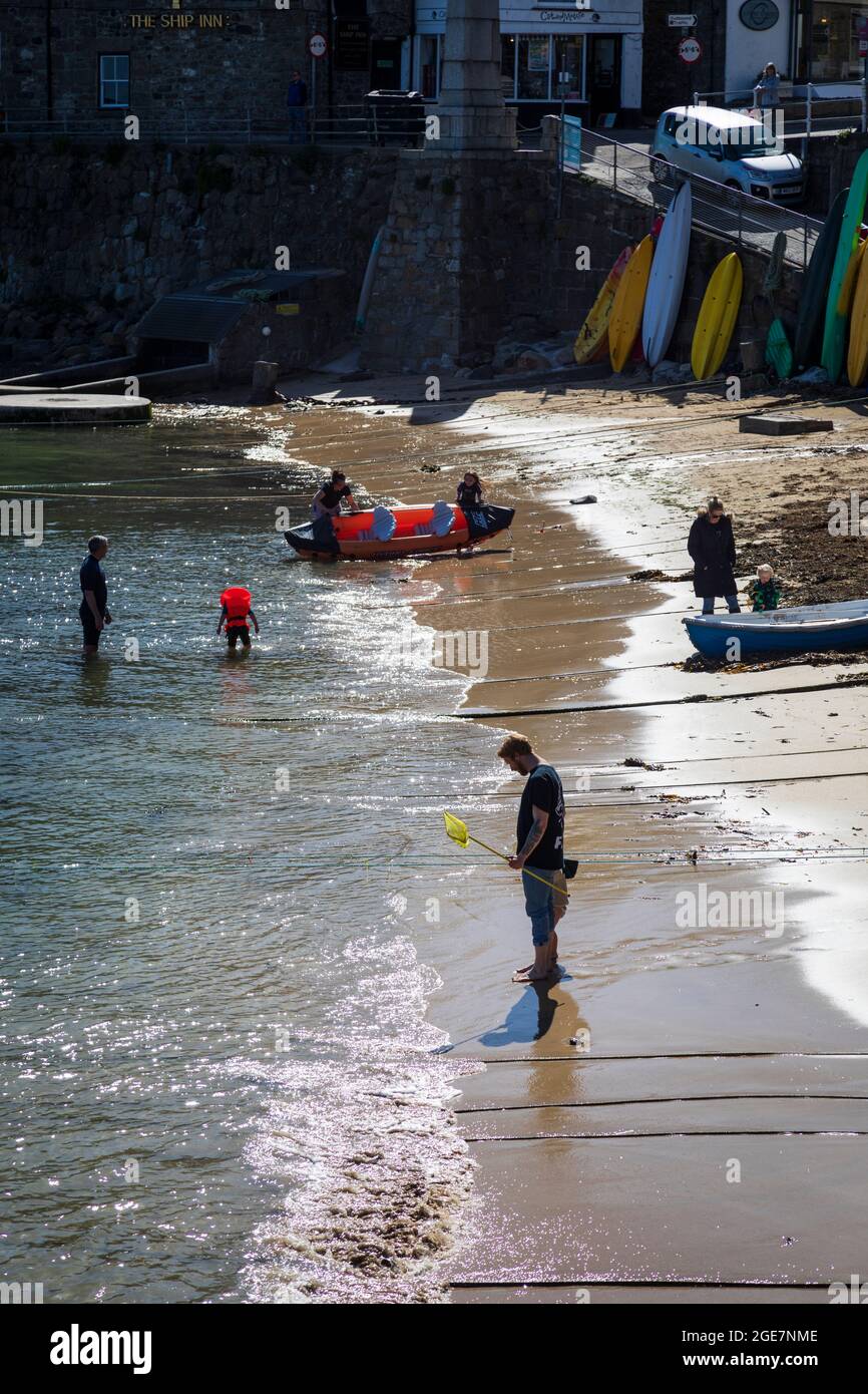 Holiday makers enjoy paddling in the sea in Mousehole harbour, Cornwall, England. Stock Photo