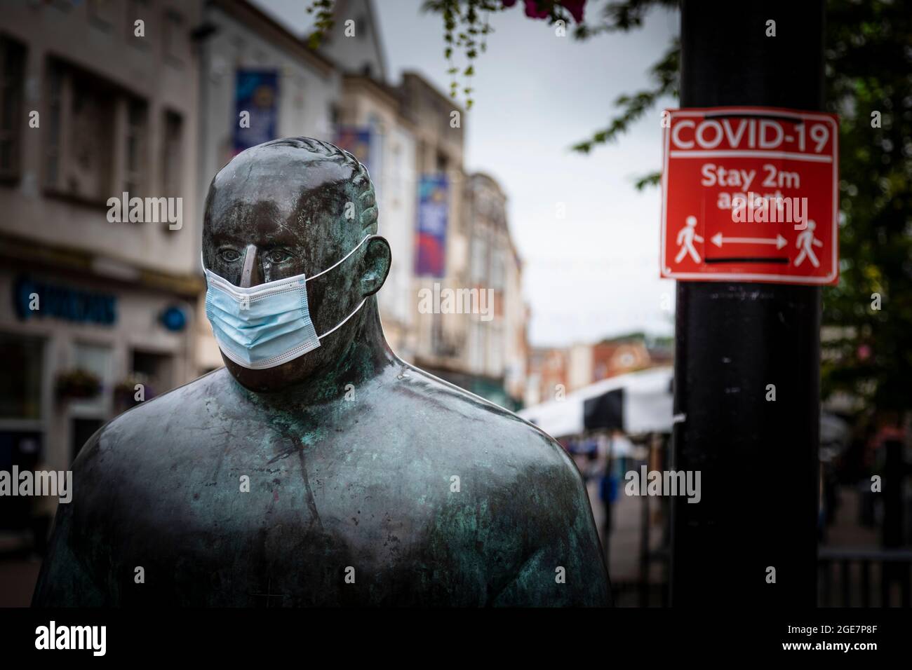 'The Sockman' by Scottish artist  Shona Kinloch represents Loughborough's hosiery industry and seen here with a face mask alongside a Covid sign durin Stock Photo