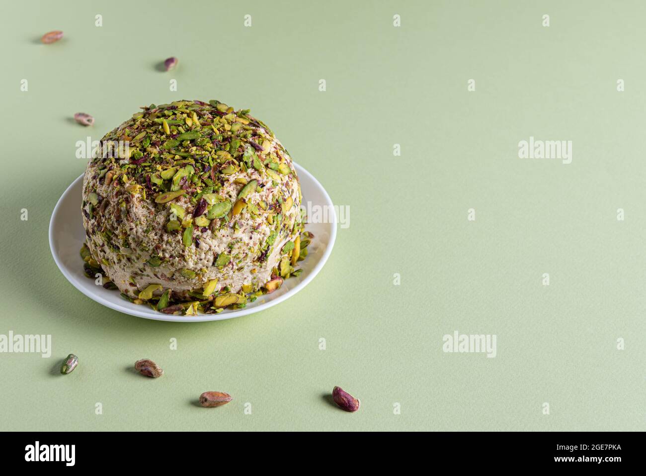 Ready to eat sesame halva with pistachios on white plate and few scattered nuts on green paper