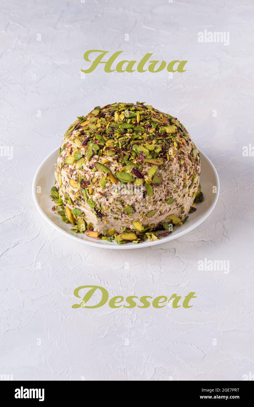 Beautiful sesame halva with pistachios nuts on textured white background with Halva dessert green text. Traditional middle eastern sweets. Jewish, tur Stock Photo