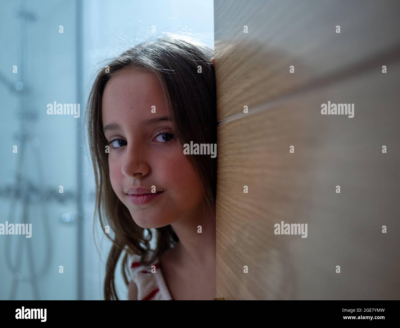 Cute little Caucasian girl looking from behind the wooden door of the