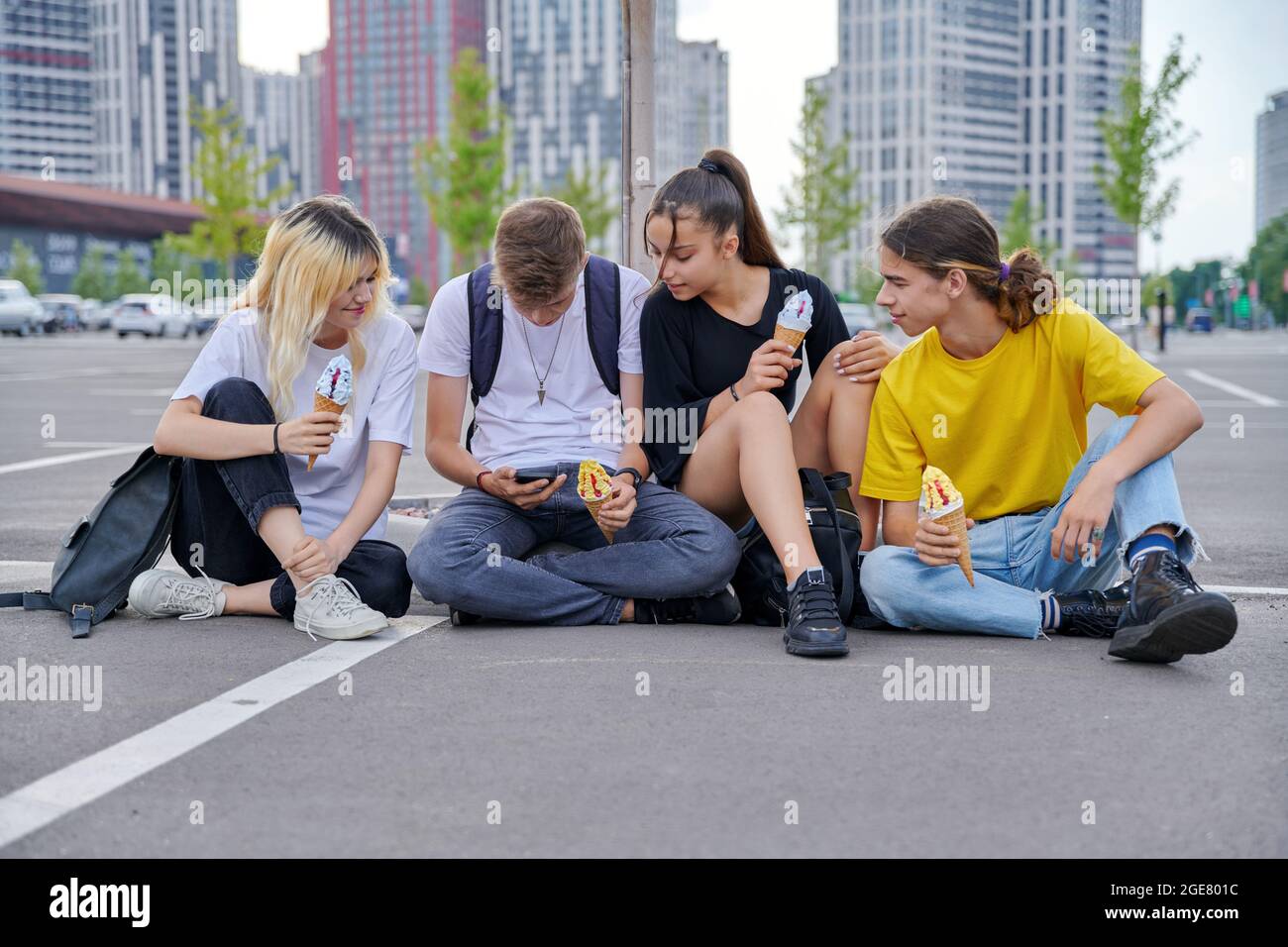 Group of teenagers with ice cream looking together at smartphone, urban style Stock Photo