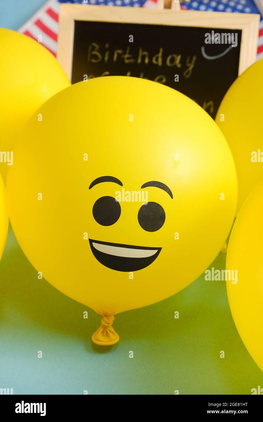 Yellow emoji balloons on the background of the board with the event inscription and American flags. Stock Photo