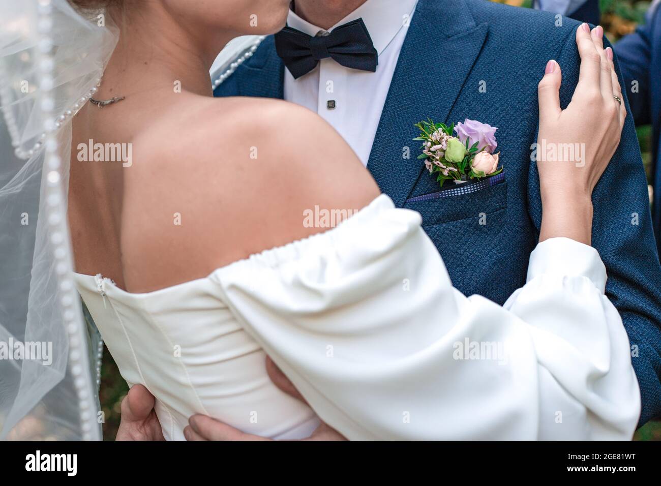 The groom in a blue suit and the bride in a white dress hug together. A woman's hand with a ring on a man's shoulder. Wedding, engagement. Love and re Stock Photo