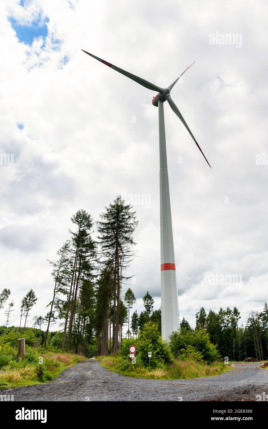 Tall wind turbine along a gravel forest road on an overcast summer day Stock Photo