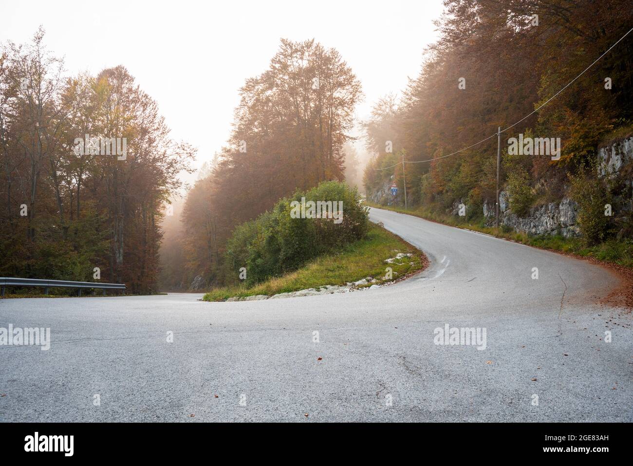 Hairpin bend along a foggy alpine road at sunset in autumn Stock Photo