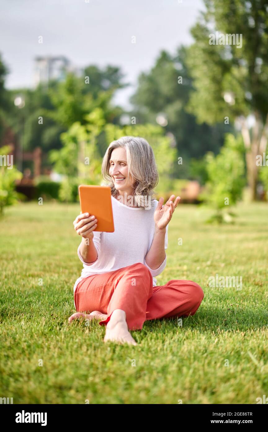 Joyful woman with tablet sitting on grass Stock Photo