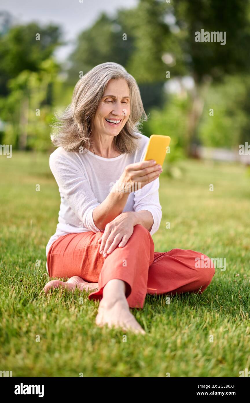 Smiling woman with smartphone sitting on grass Stock Photo