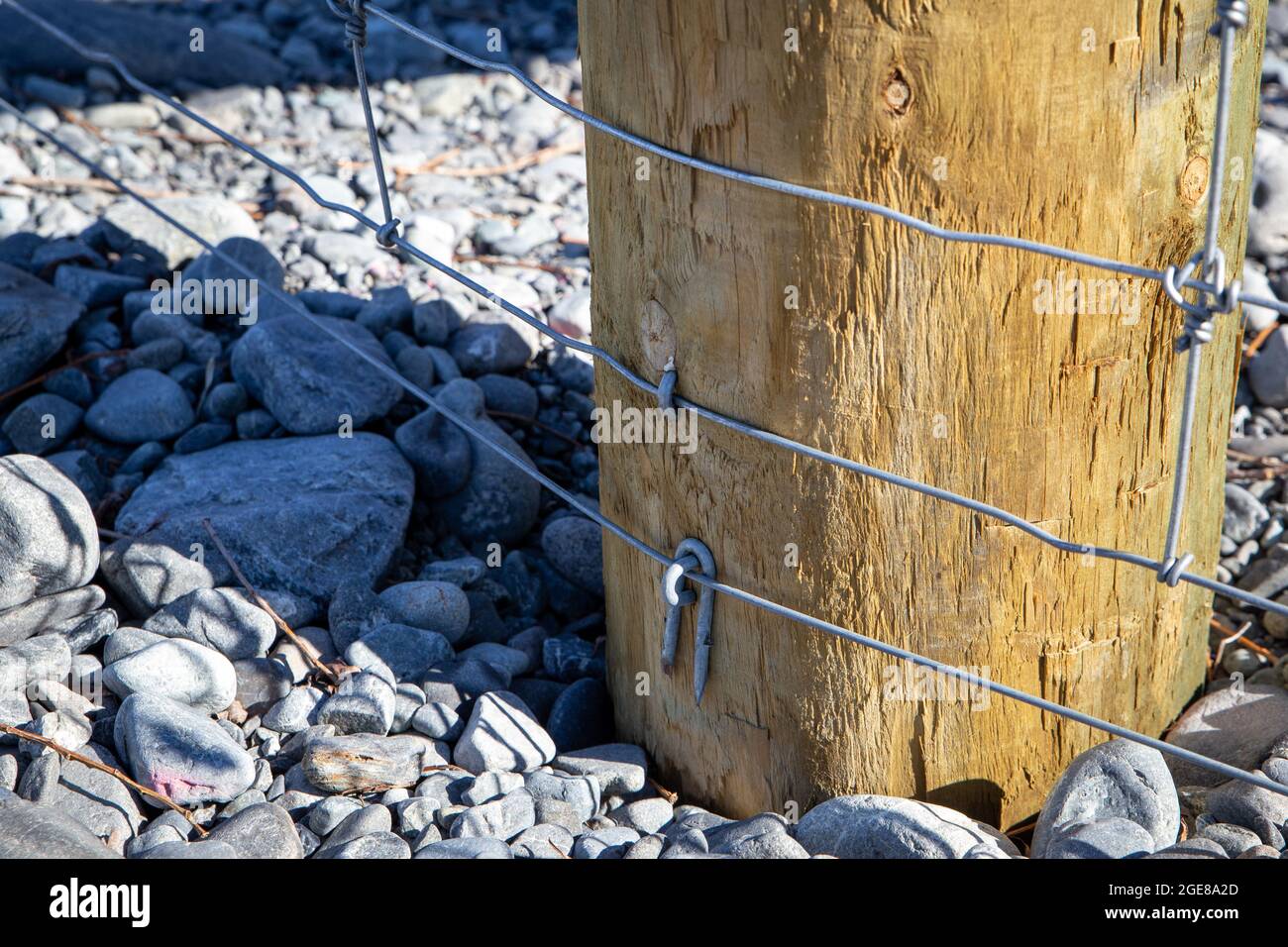 Close up of components of a post and netting farm fence along the border of the farm and river bed, Canterbury, New Zealand Stock Photo
