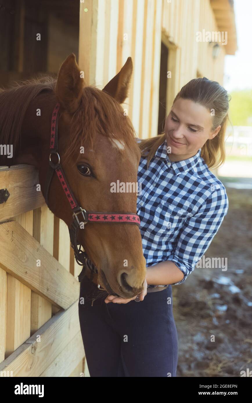 Female horse owner standing at the horse stable embracing a dark bay ...