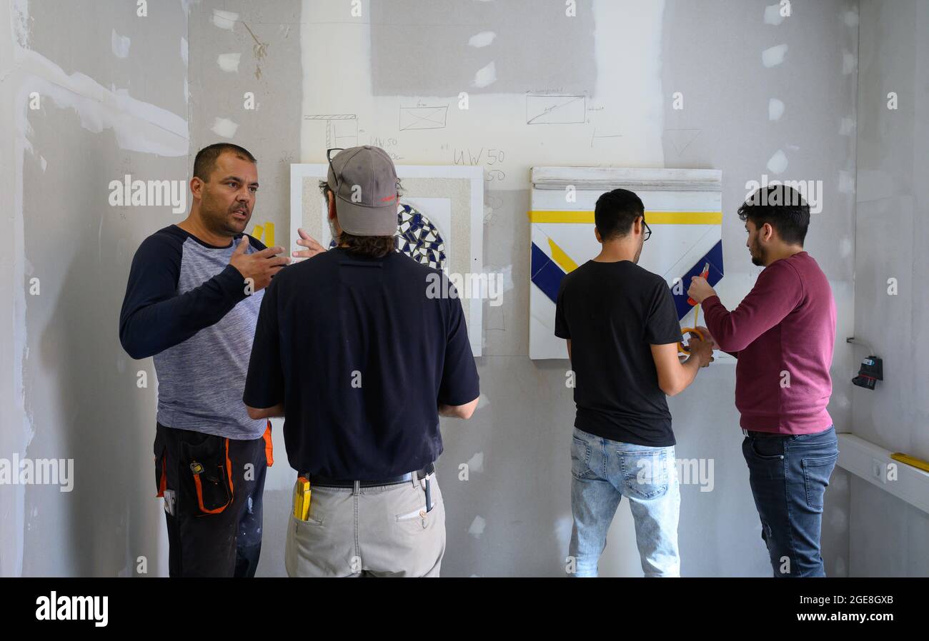 11 August 2021, Saxony, Dresden: Michael Hanke (left), branch manager and trainer at the training provider LOESERnet.com GmbH, explains surface coating on practice fields to participants in the pilot course for refugees in the learning workshops. In the BAMF (Federal Office for Migration and Refugees) support project, refugees who have already fallen through the cracks are taught German in a particularly practical way in workshops. In special language courses, migrants can learn practical vocabulary from everyday life as a craftsman - and at the same time practice in various trades.(to dpa 'Le Stock Photo