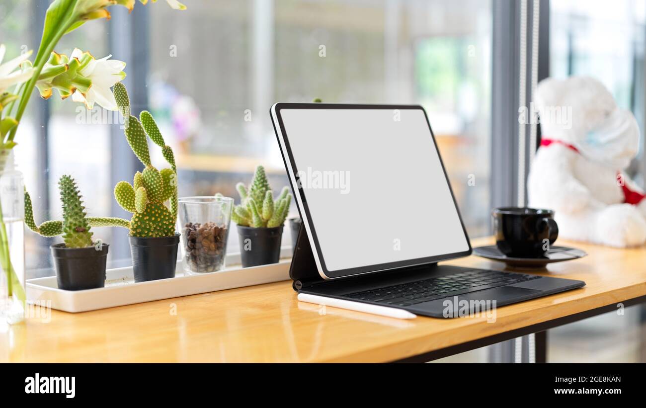 Smart tablet blank screen mockup on wooden desk with cactus, coffee cup and blurred window glass in the background Stock Photo