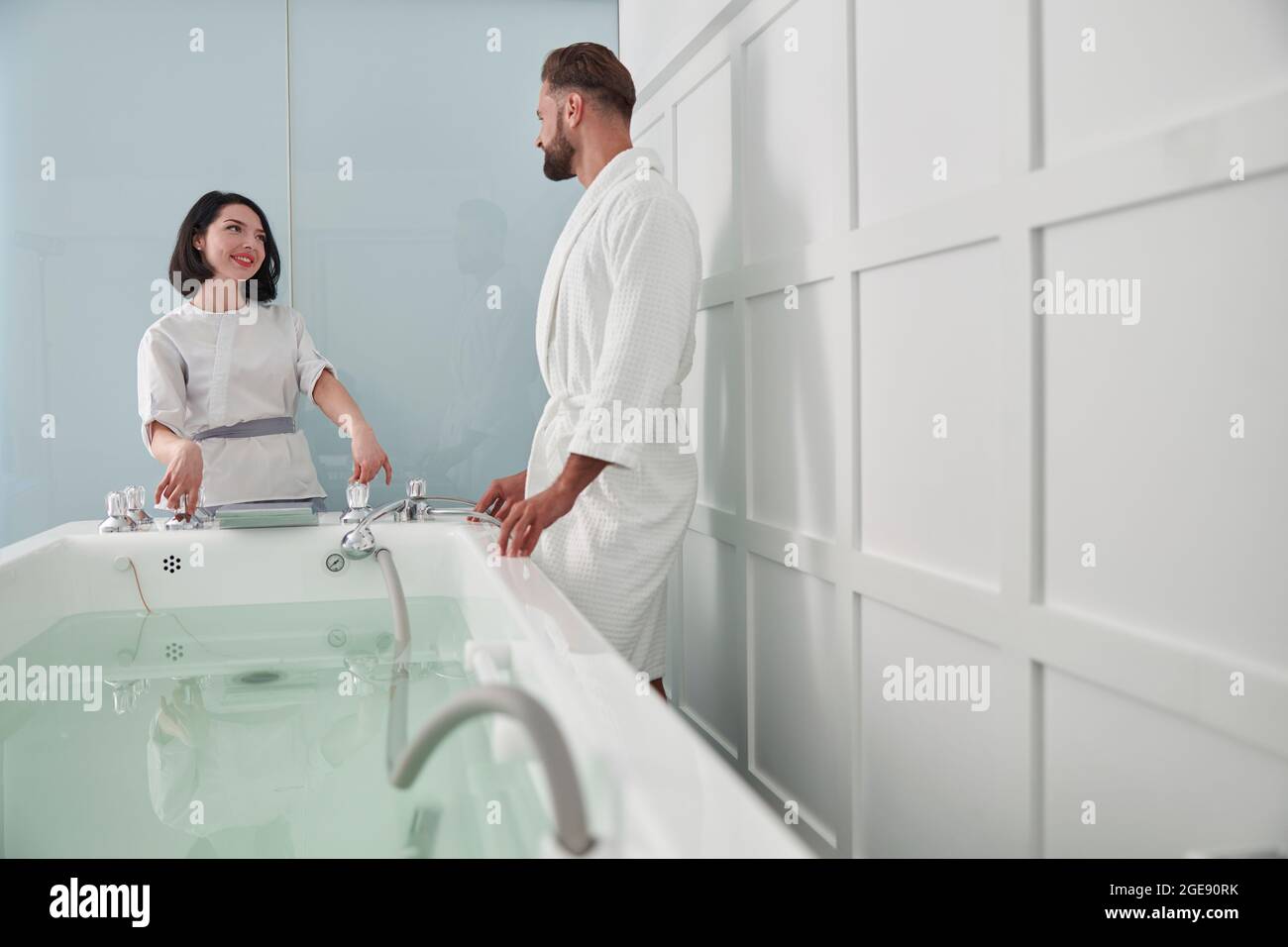Woman in uniform shows hydro massage bath to man guest in modern salon Stock Photo