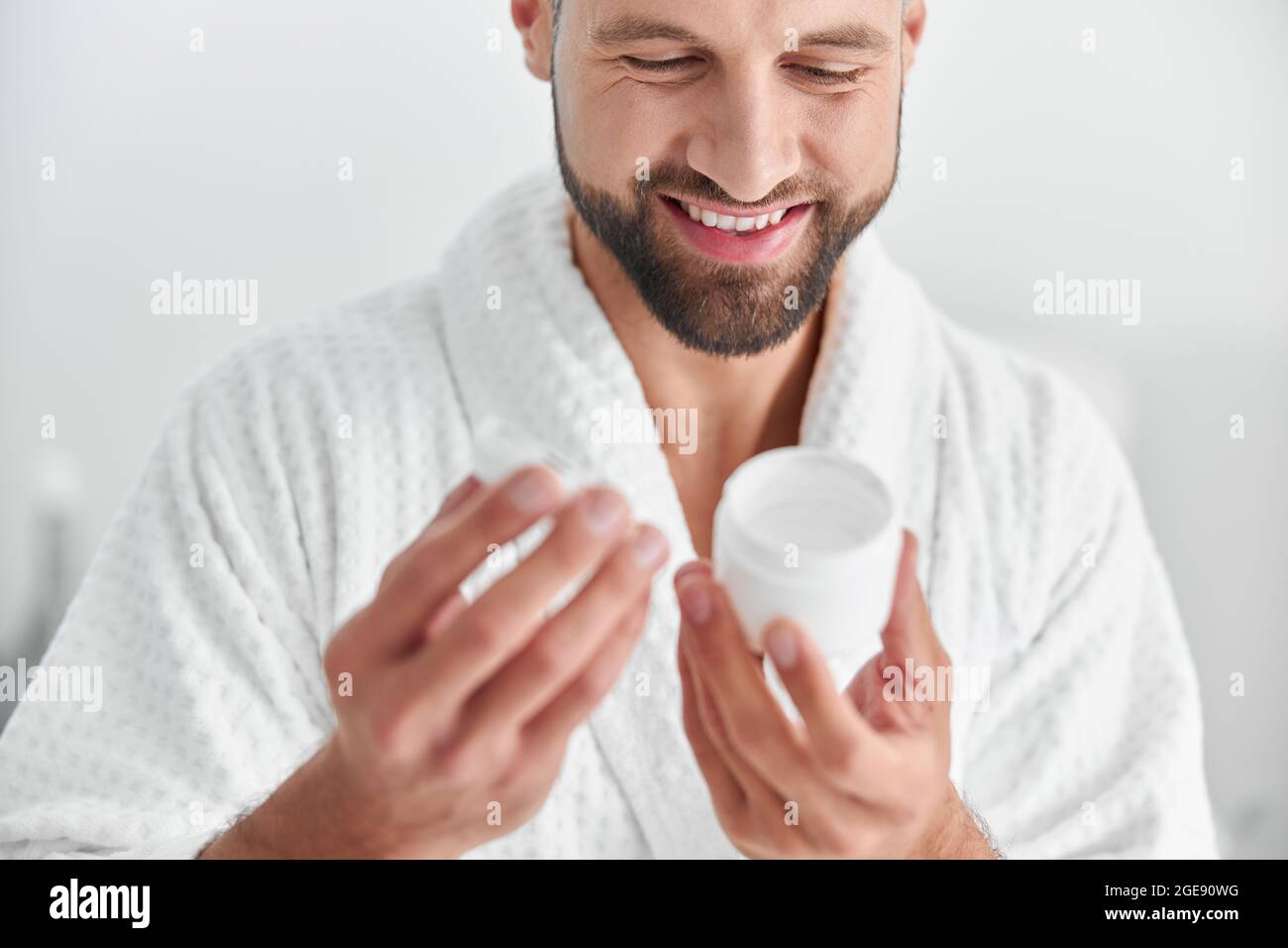 Happy mature man looks at open jar of cream in professional cosmetologycal clinic Stock Photo