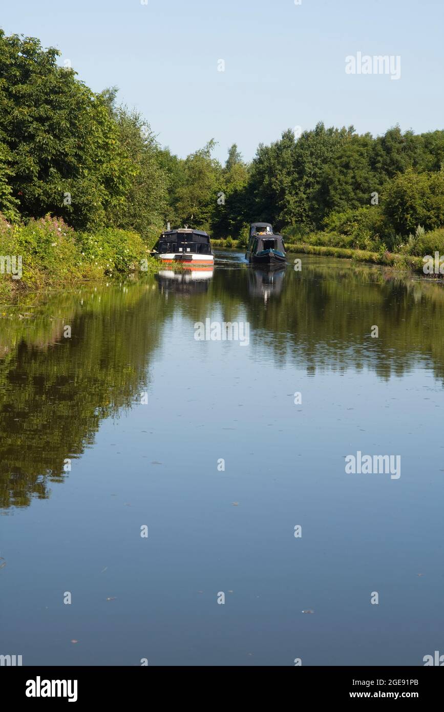 A narrowboat passes a moored widebeam boat on a bend near Burscough on the Leeds & Liverpool canal Stock Photo