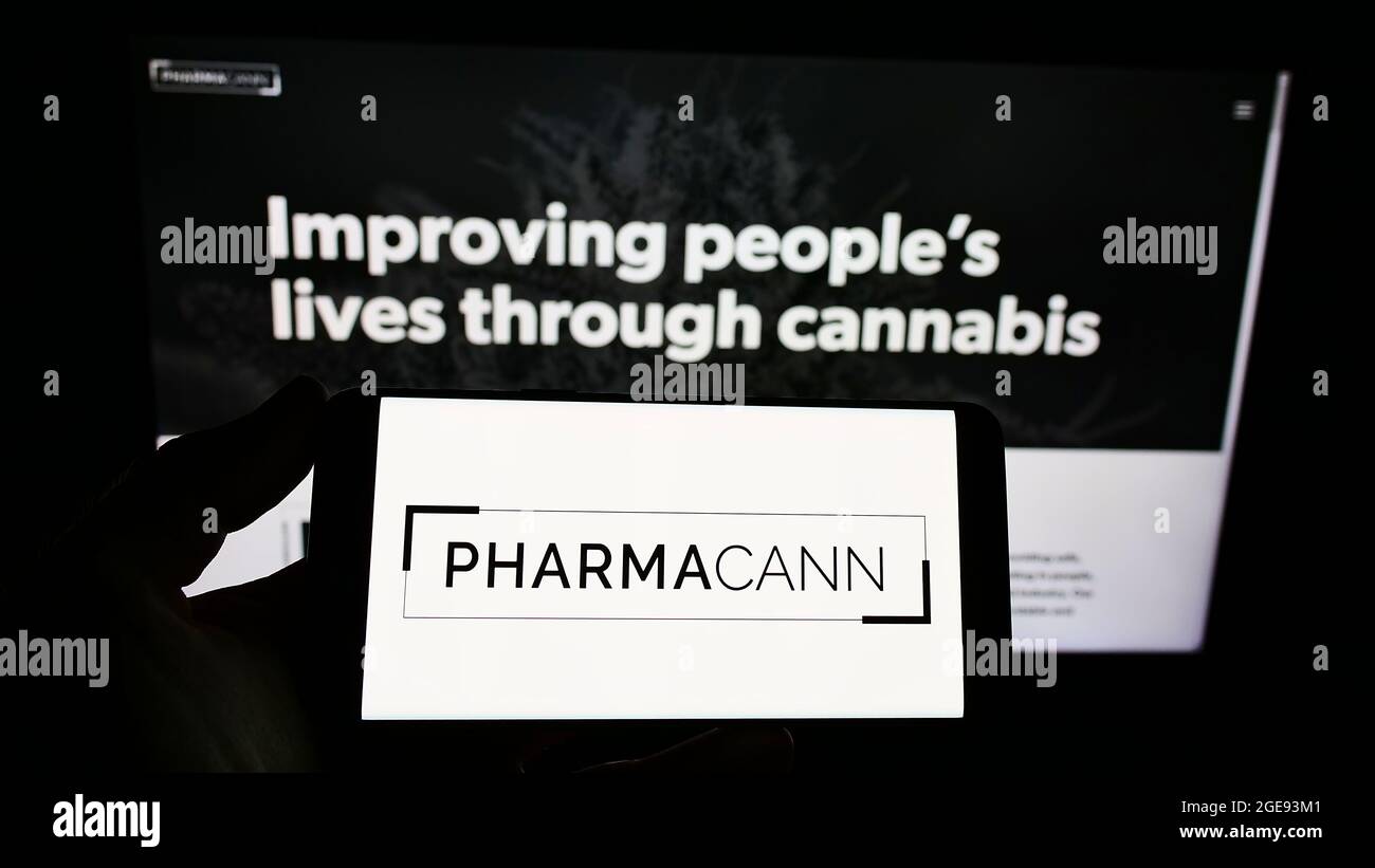 Person holding smartphone with logo of US cannabis company PharmaCann Inc. on screen in front of website. Focus on phone display. Stock Photo