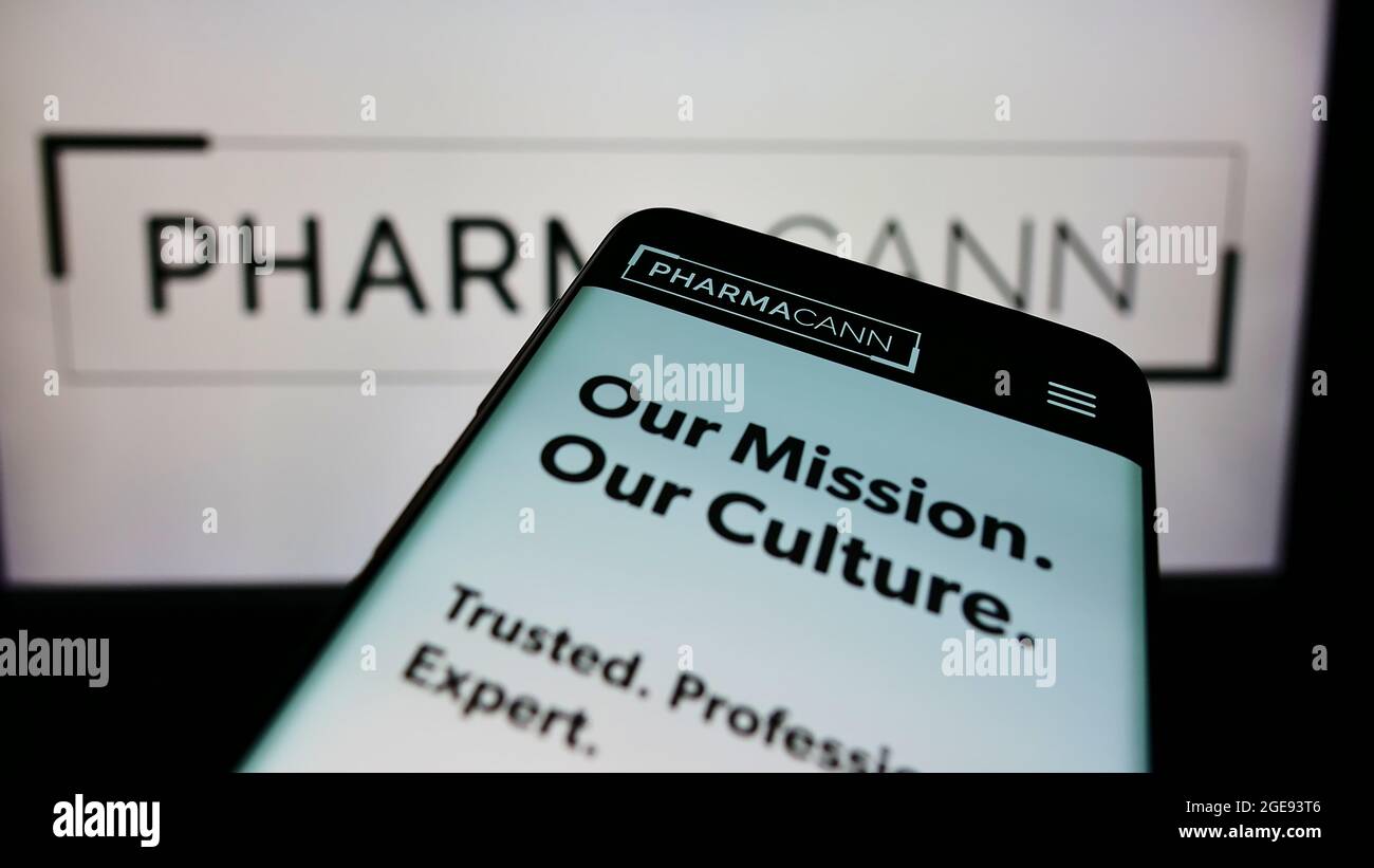 Mobile phone with webpage of American cannabis company PharmaCann Inc. on screen in front of business logo. Focus on top-left of phone display. Stock Photo