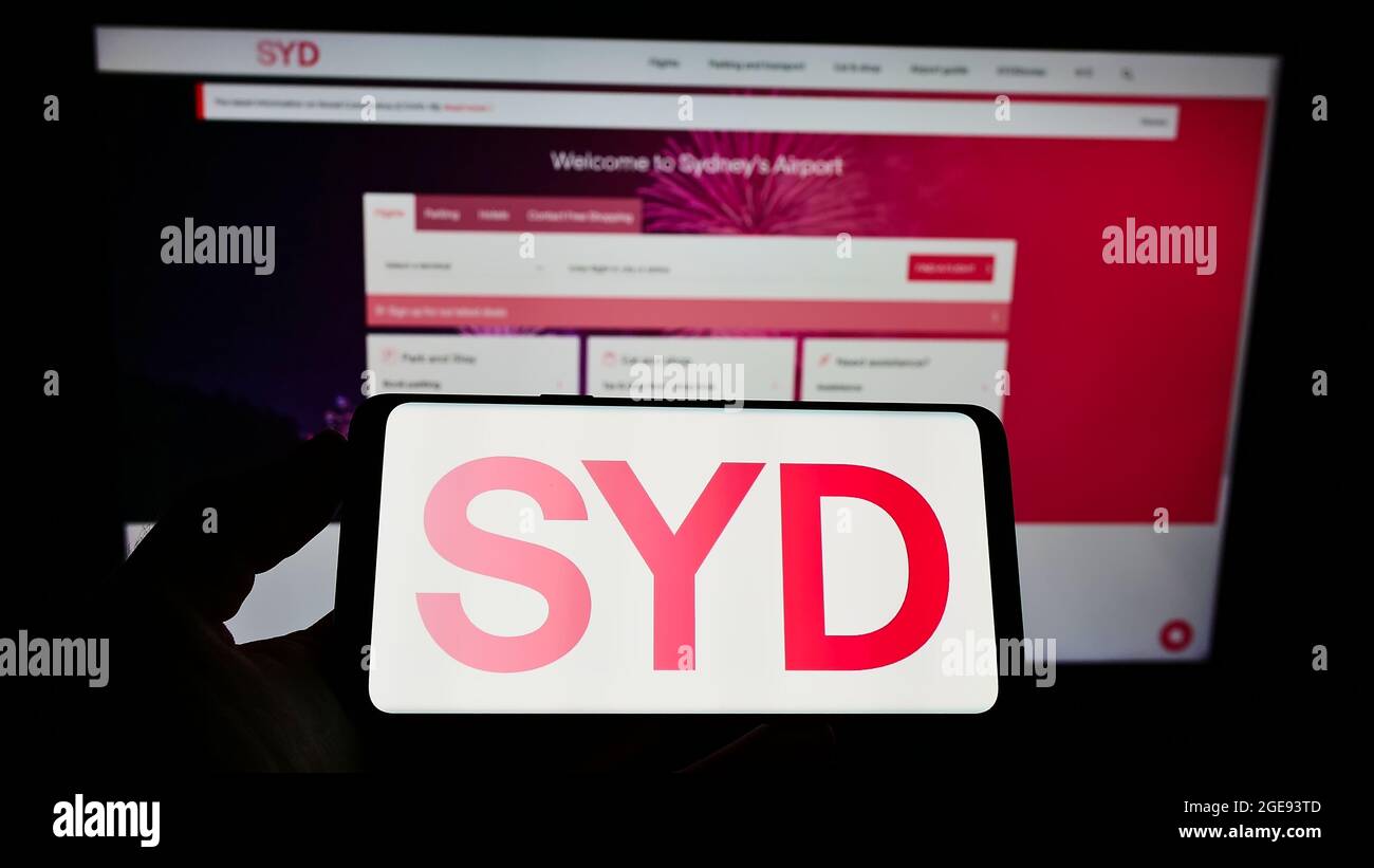 Person holding smartphone with logo of Australian company Sydney Airport Holdings Pty Ltd on screen in front of website. Focus on phone display. Stock Photo