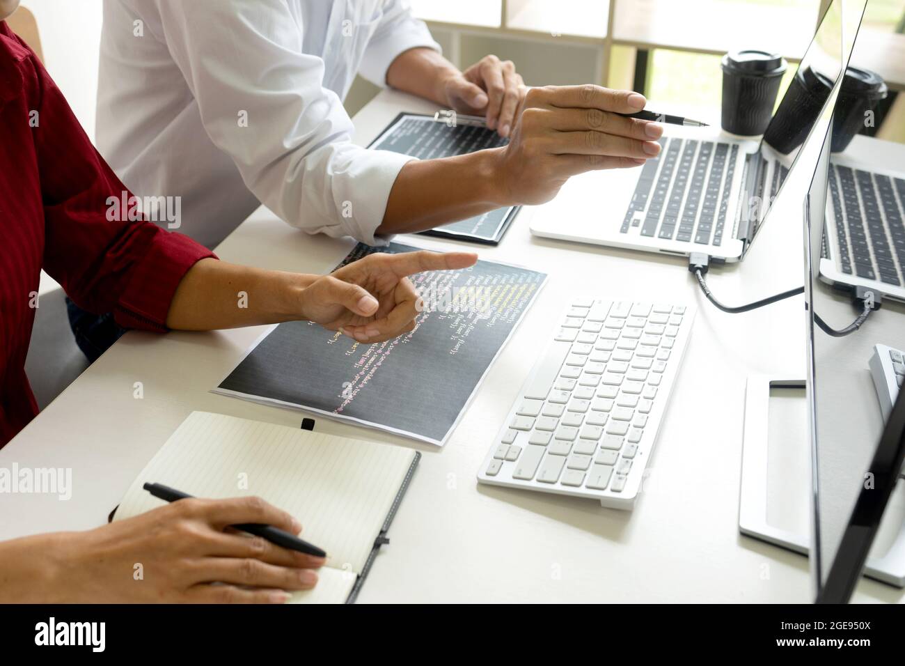 Two programmers are discussing on creen work with computer code paper on office table. Stock Photo