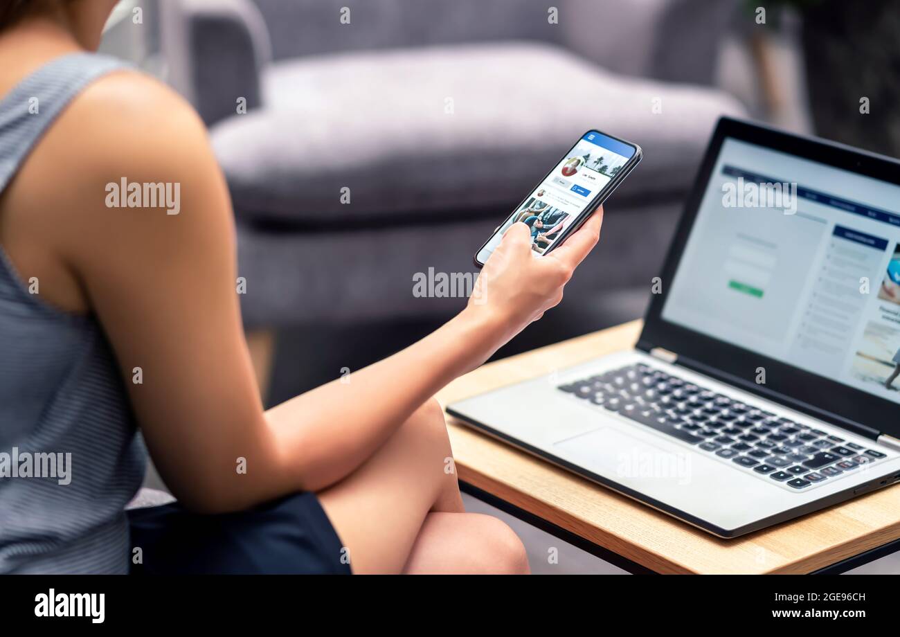 Social media profile page in smartphone screen at work. Woman looking at feed, status update or post with mobile phone. Inefficient lazy worker. Stock Photo