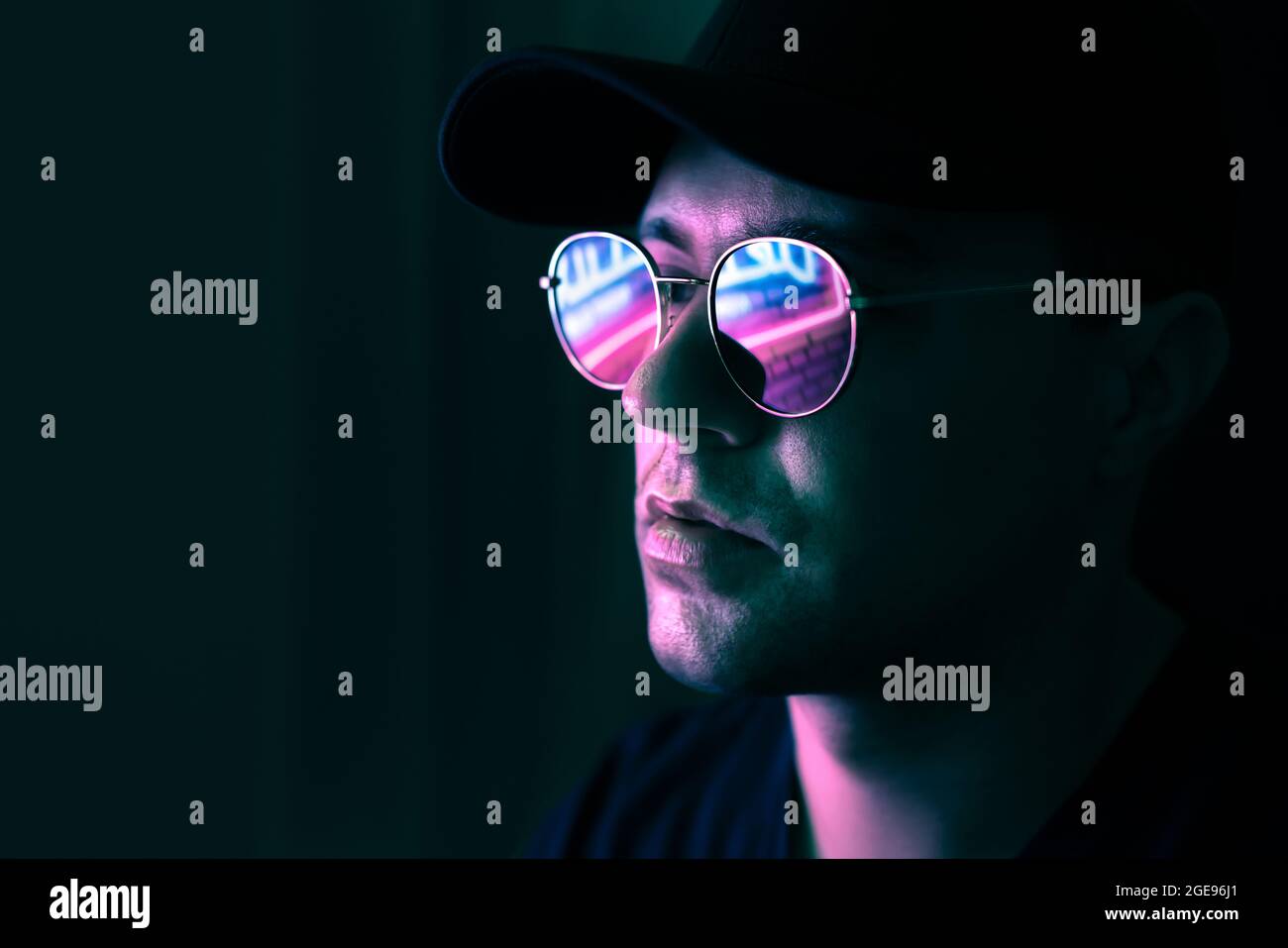 Neon reflection in glasses. Man in fluorescent light from city led sign. Mysterious cool model in futuristic cyberpunk portrait. Guy in sunglasses. Stock Photo