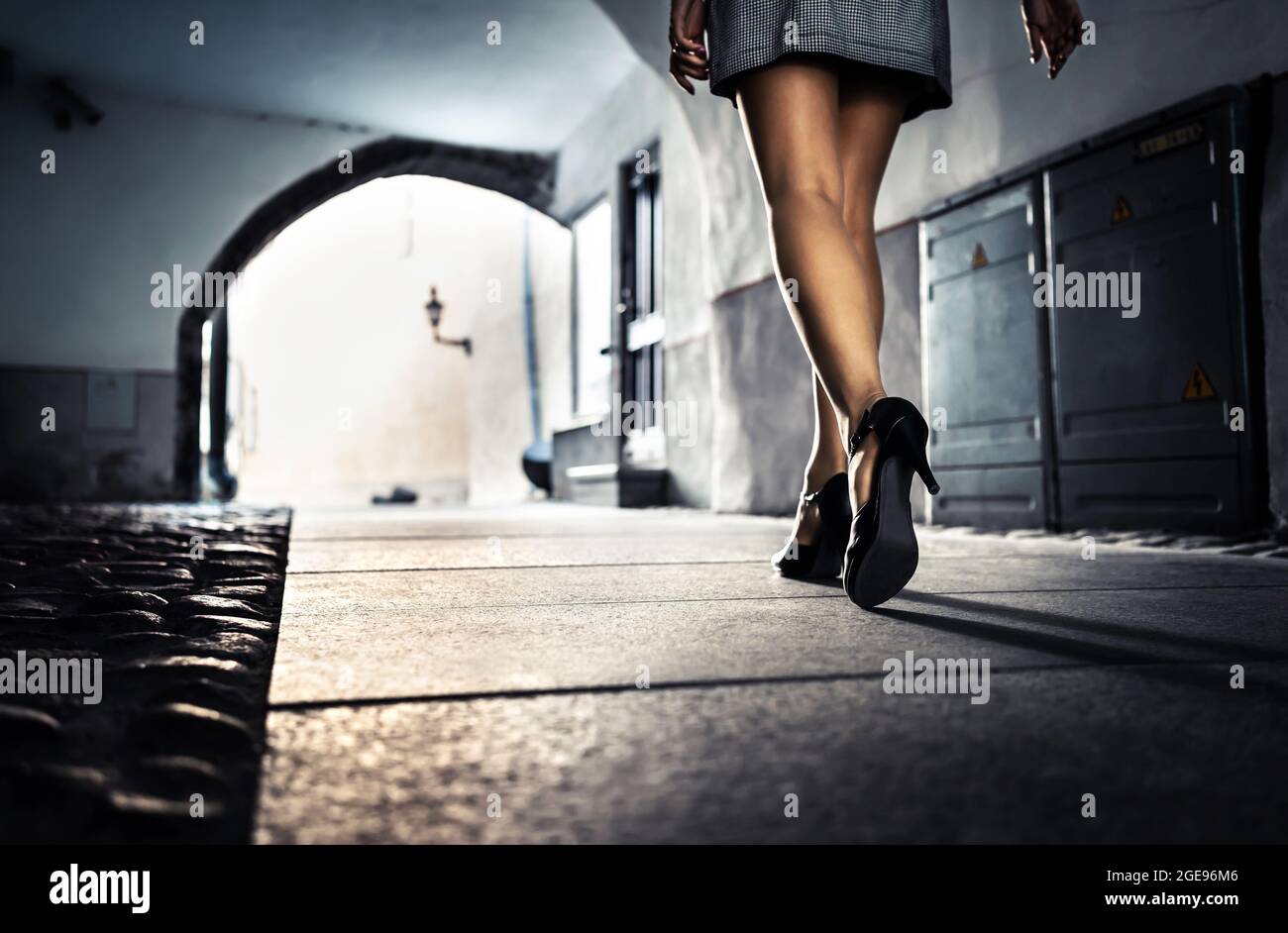 Woman in dark alley and city street at night alone. Lonely scared girl walking, afraid of sexual harassment or robber following. Scary dramatic tunnel. Stock Photo