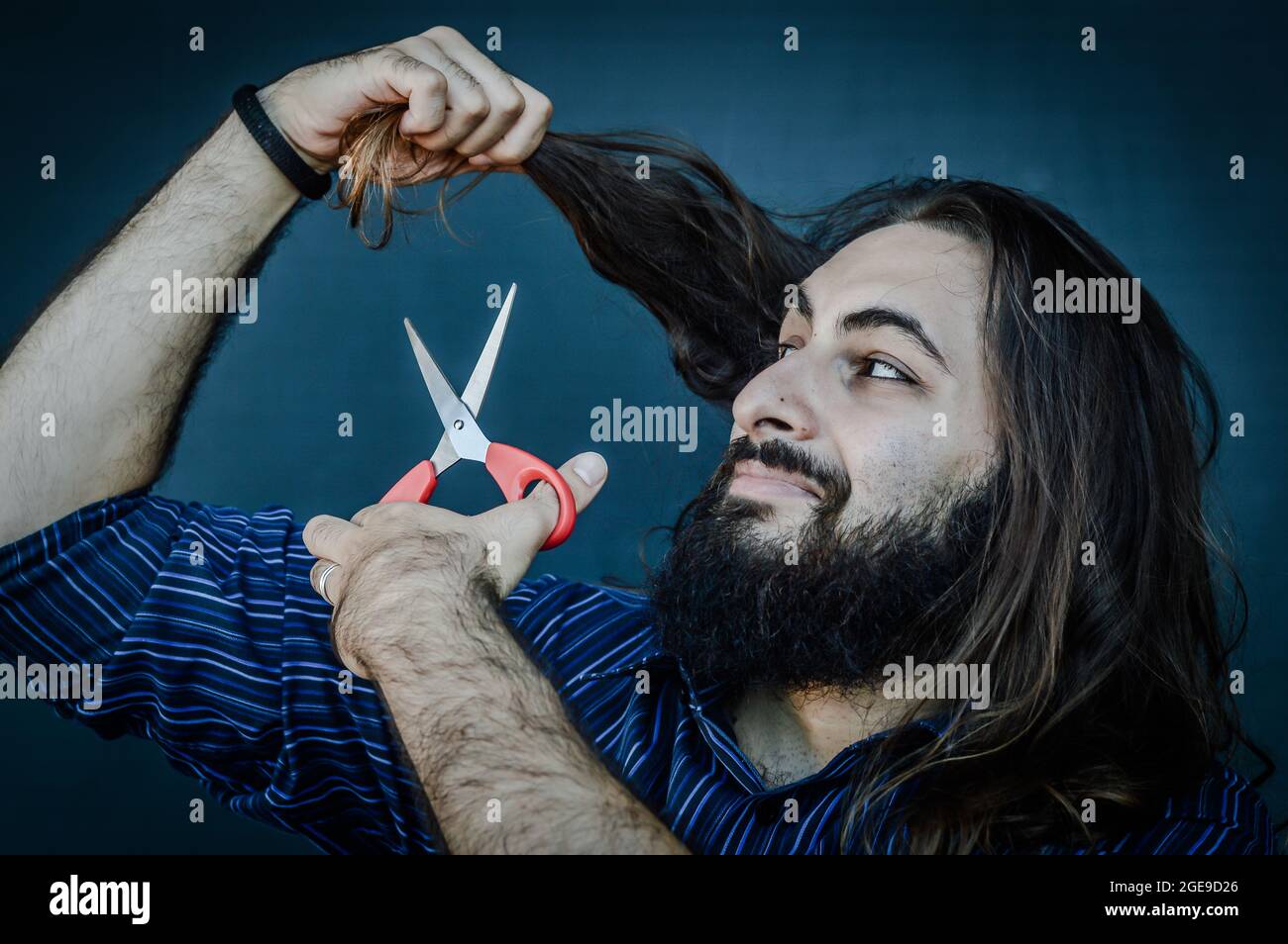 portrait of a young man with a beard and long hair who, with a scissor