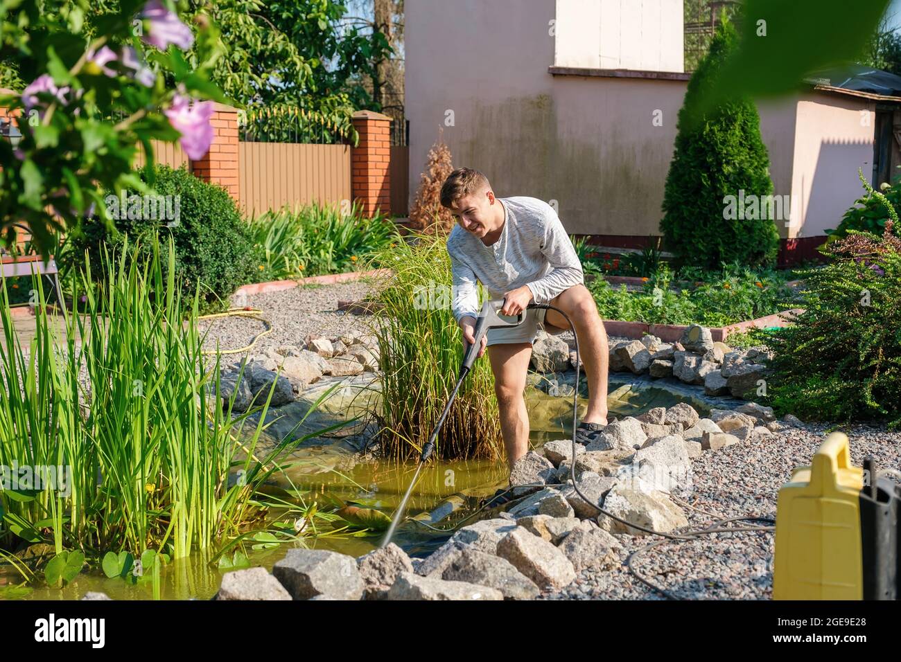 man cleans garden pond bottom with high-pressure washer from mud and sludge. Stock Photo