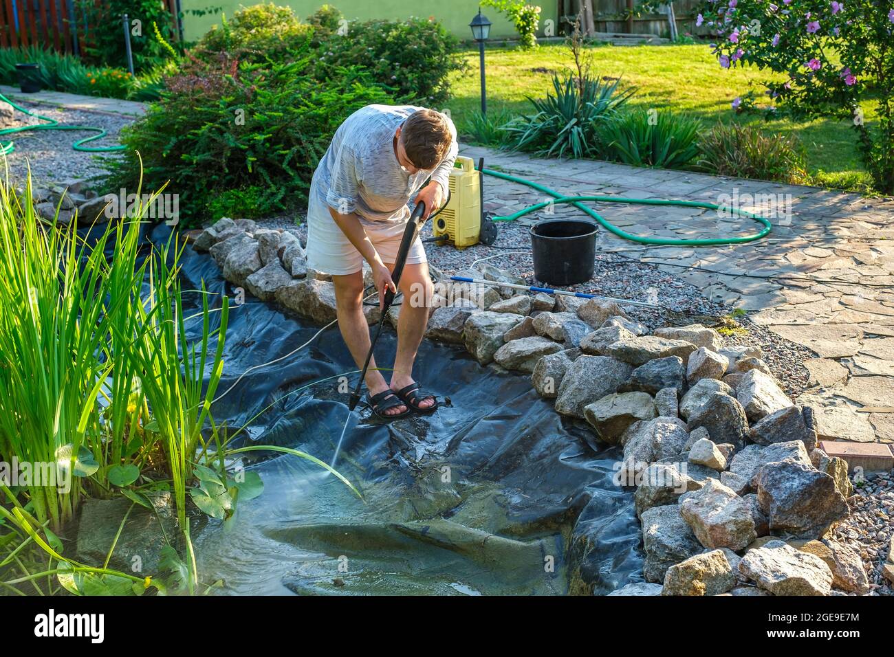 Man cleans garden pond bottom landing net from mud, sludge and water