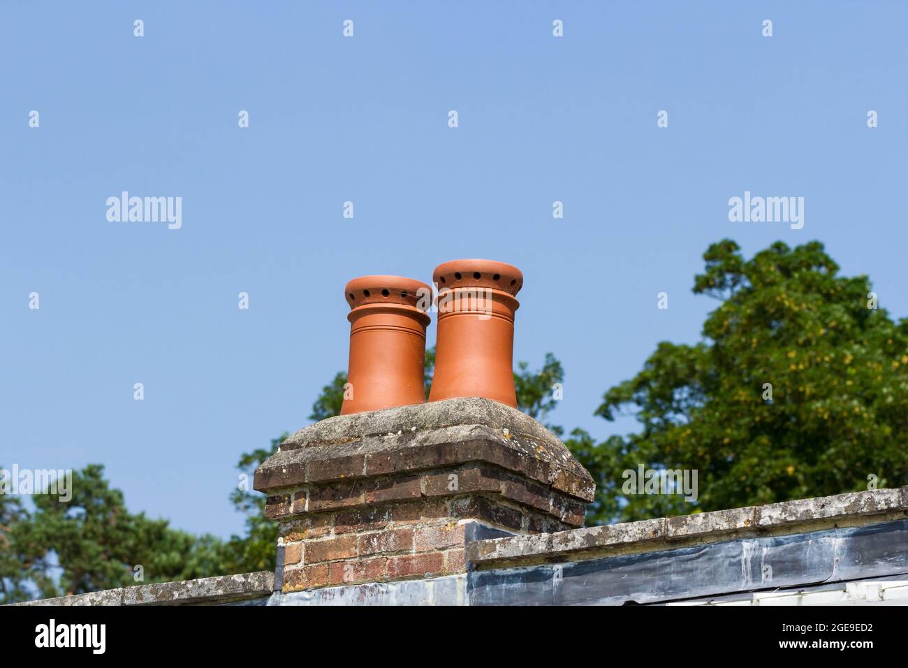 Two terracotta chimney pots against a blue sky UK Stock Photo