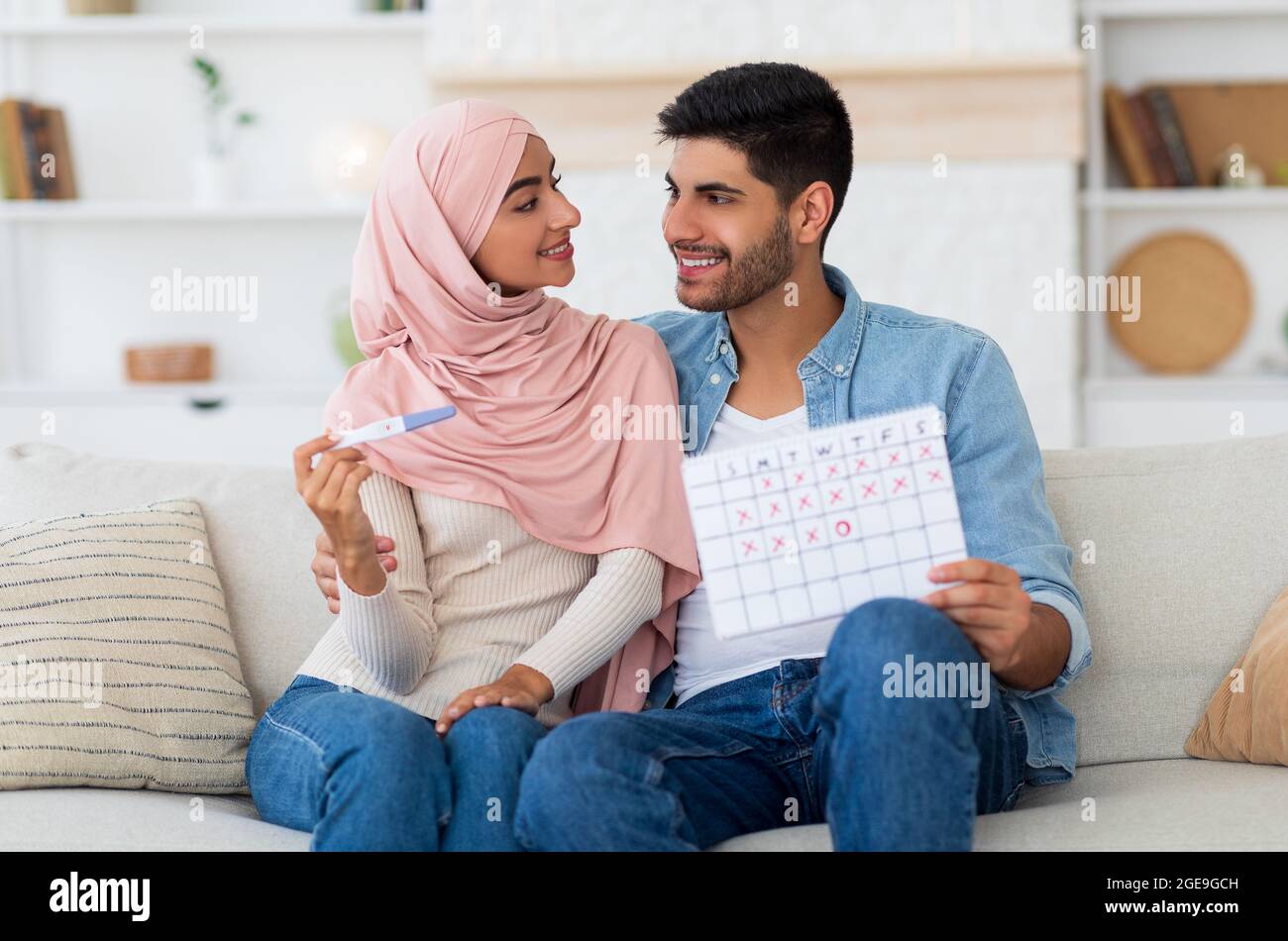 Happy arab couple planning pregnancy, holding positive pregnancy test and ovulation calendar