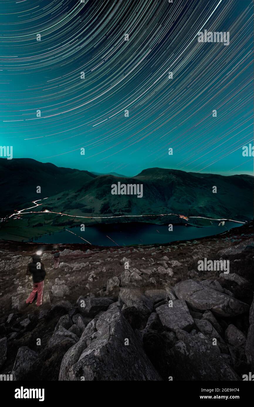 A person looking at star trails over Buttermere lake in Lake District, UK.Night under the stars concept. Stock Photo