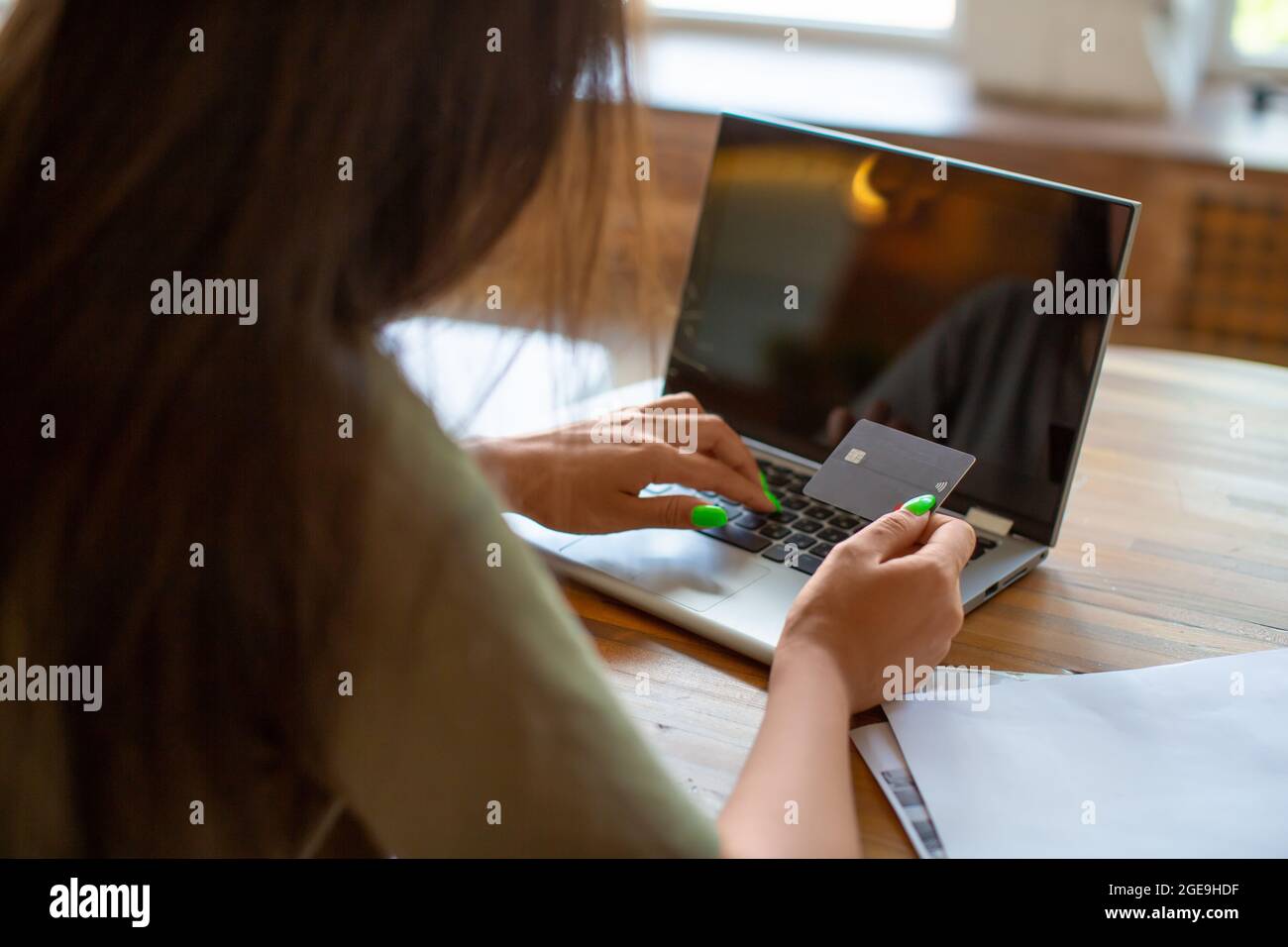 Back view of a woman with credit card in hands in front of laptop monitor. Online shopping at home concept. Stock Photo