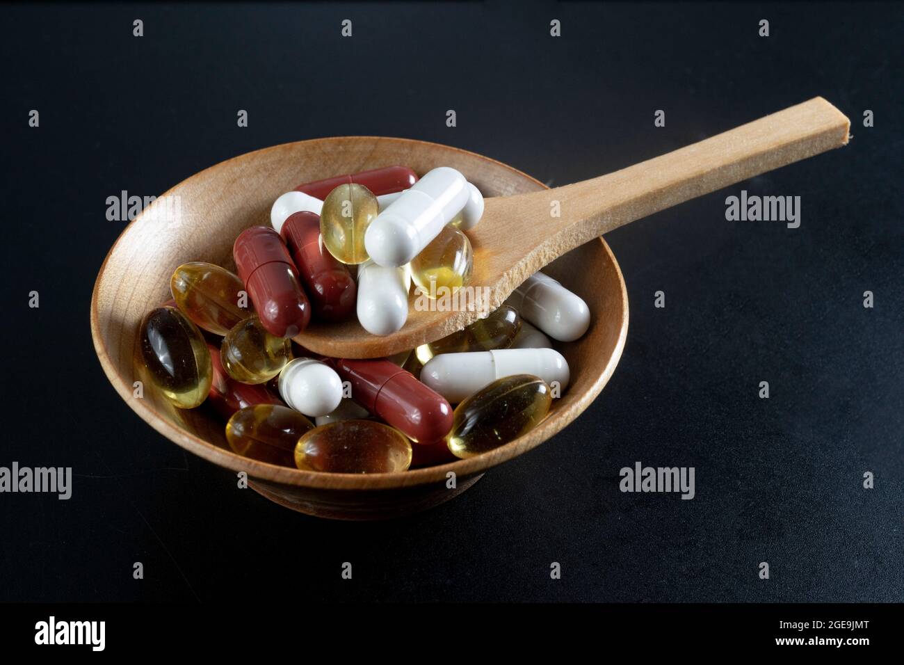 different pills and capsules on a wooden bowl with a bamboo spoon, isolated on black background. Stock Photo