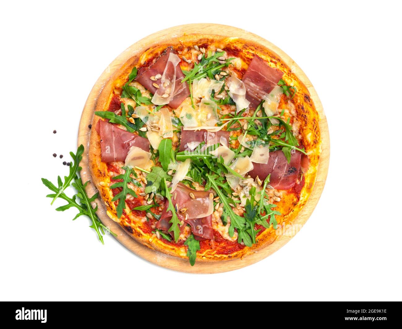 High angle view of pizza with dry cured ham, parmesan cheese, rocket leaves and ipne nuts on wooden platter, isolated on white background Stock Photo
