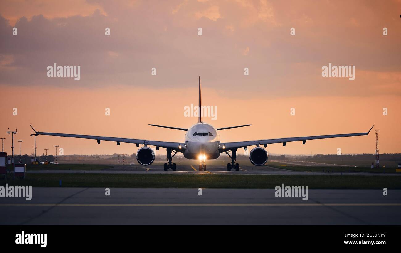 Wide-body airplane taxiing for take off. Front view of plane against airport at sunset. Stock Photo