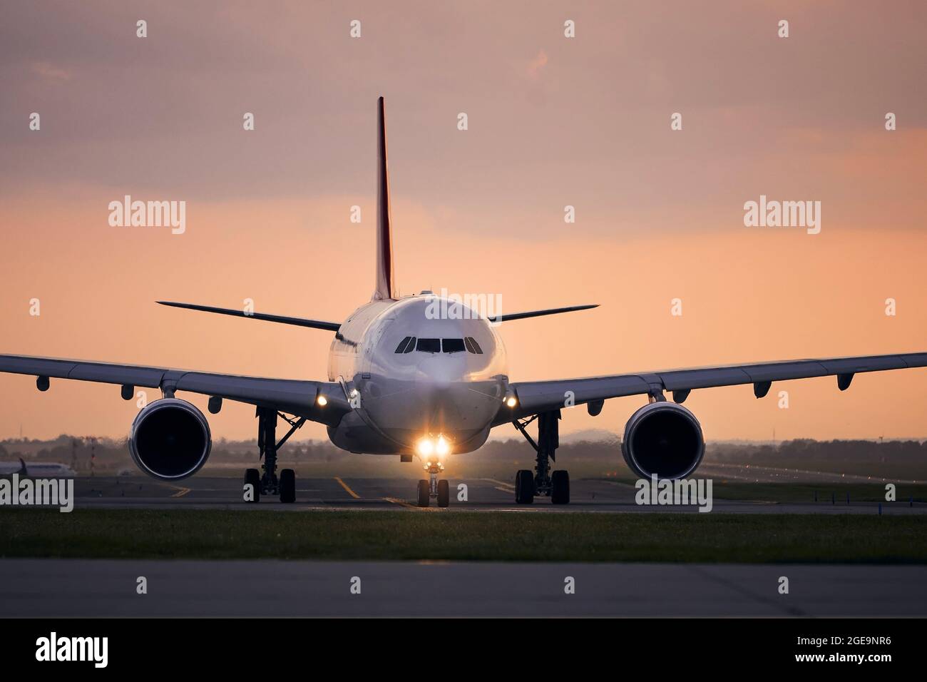 Wide-body airplane taxiing for take off. Front view of plane against airport at sunset. Stock Photo