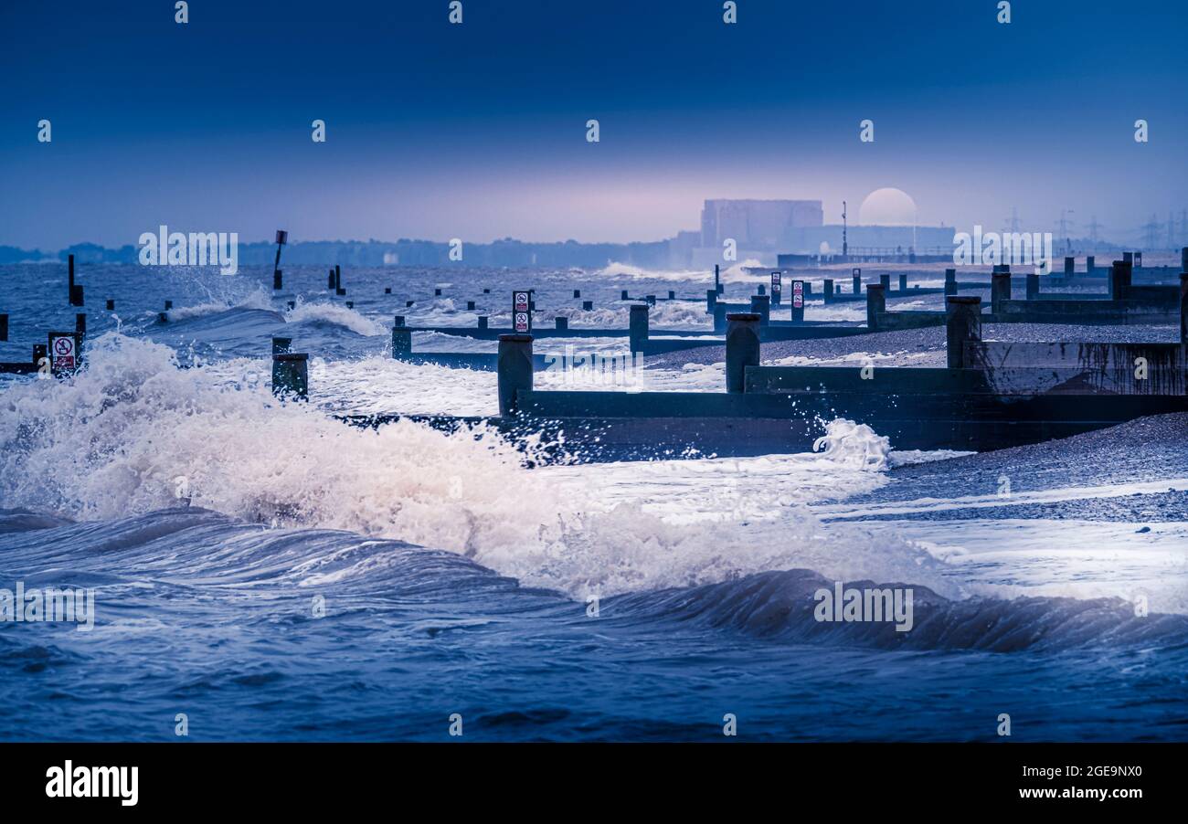 Waves break on the beach and groynes at Southwold with Sizewell nuclear power station in the distance. Stock Photo