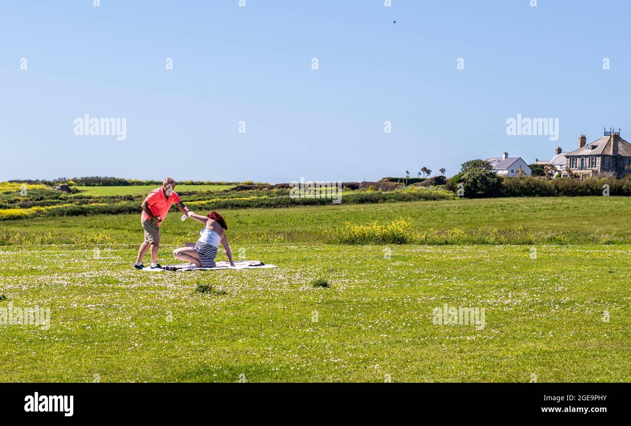 Man helping woman up from picnic in The Lizard in Cornwall in England. Stock Photo