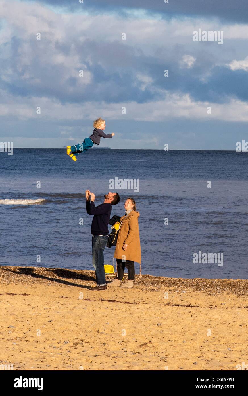 Family on beach with father throwing child mid air in Southwold in Suffolk in England. Stock Photo