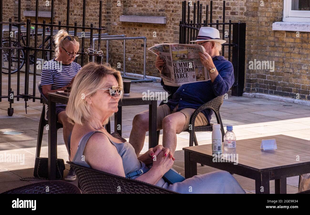 A man reading a newspaper and a woman looking at her phone and another woman wearing sunglasses looking in the distance in Sloane Square in Central London. Stock Photo