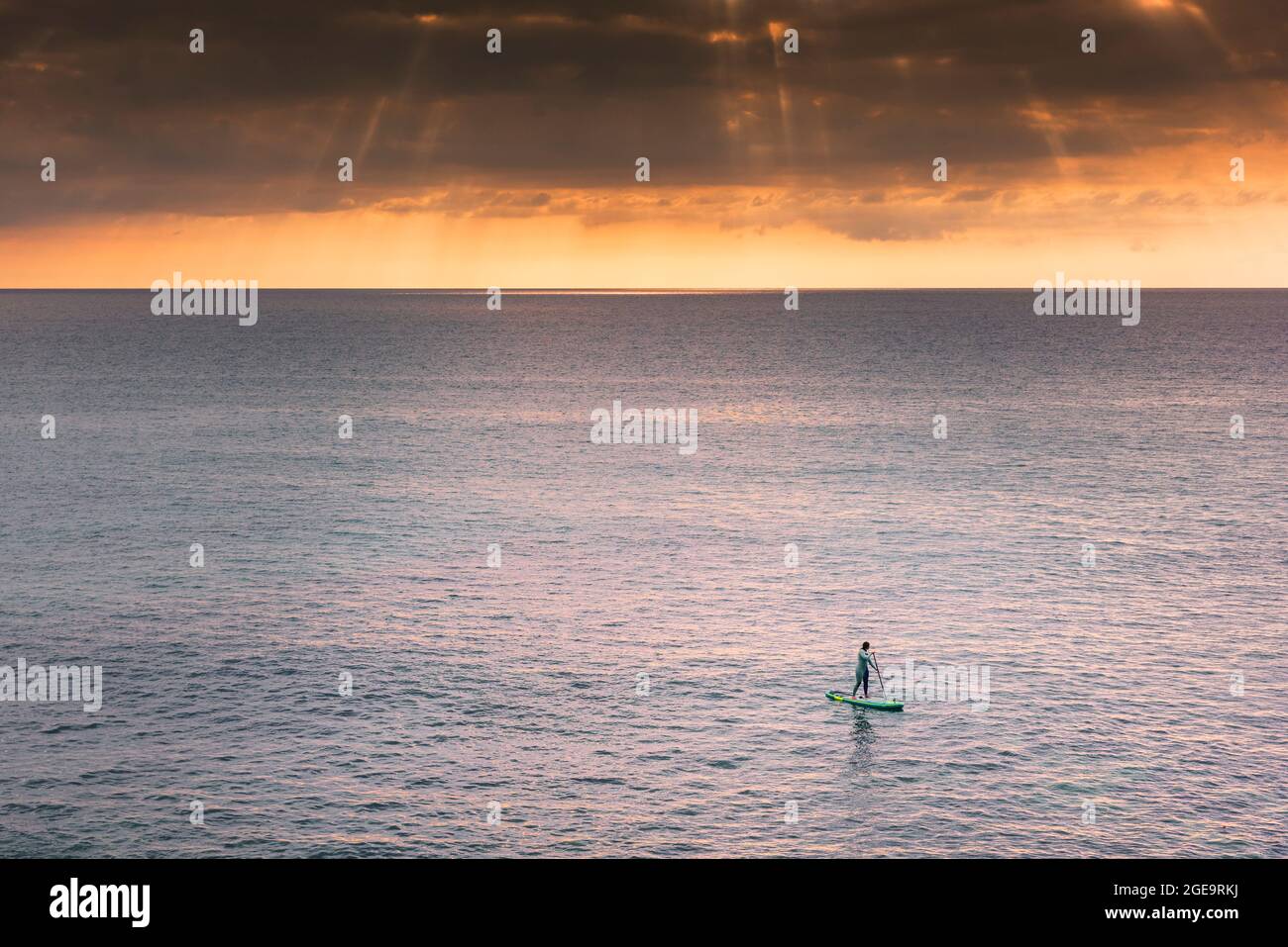 A holidaymaker on a stand up paddleboard in the sea as the sun sets over Fistral Bay in Newquay in Cornwall. Stock Photo