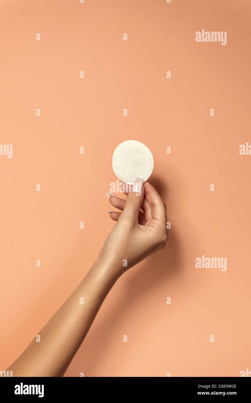 Crop unrecognizable Woman with manicure and delicate skin demonstrating clean cotton pad on beige background Stock Photo
