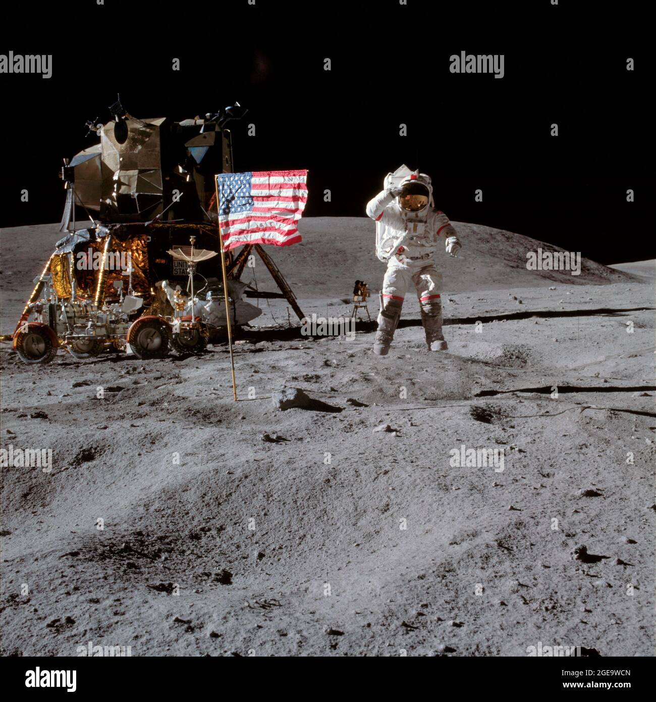 Astronaut John W. Young, commander of the Apollo 16 lunar landing mission, leaps from the lunar surface as he salutes the United States flag at the Descartes landing site during the first Apollo 16 extravehicular activity (EVA). Astronaut Charles M. Duke Jr., lunar module pilot, took this picture. The Lunar Module (LM) 'Orion' is on the left. The Lunar Roving Vehicle (LRV) is parked beside the LM. The object behind Young (in the shade of the LM) is the Far Ultraviolet Camera/Spectrograph (FUC/S). Stone Mountain dominates the background in this lunar scene. Stock Photo