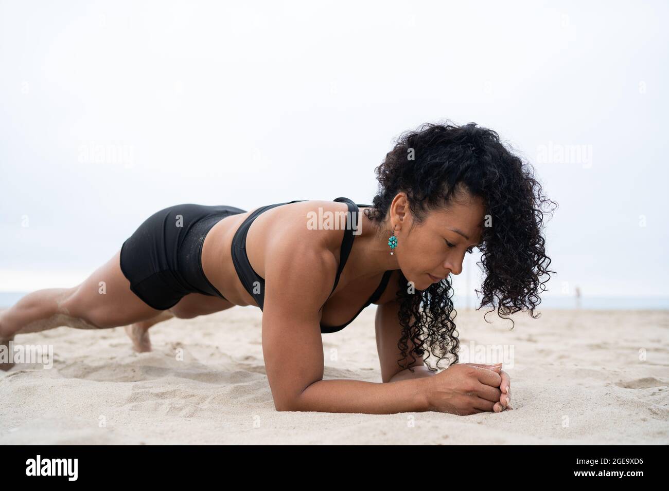 Side view of fit female athlete doing plank exercise while training on sandy shore Stock Photo