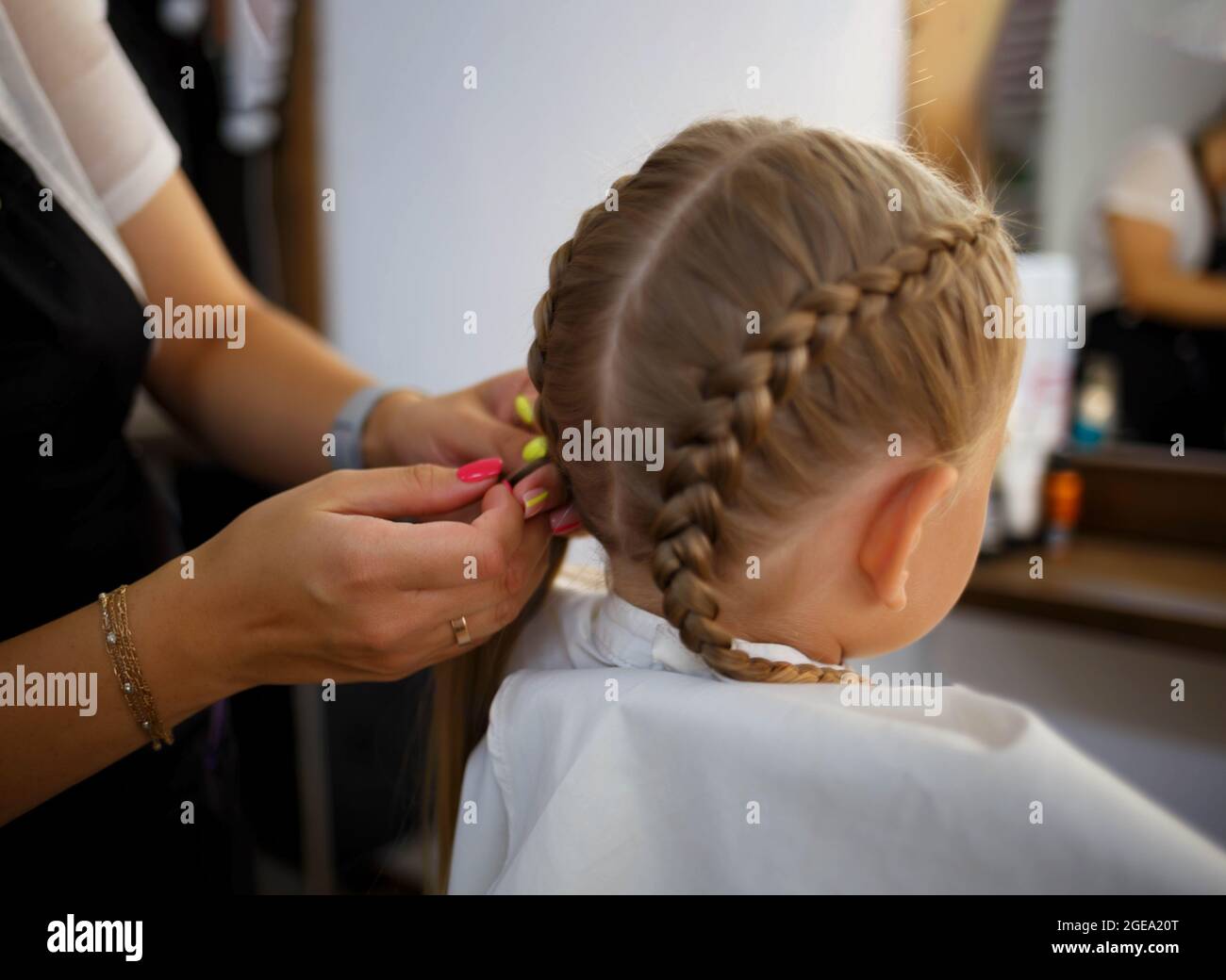 the little girl in the barber chair the hairdresser weaves a braid. Stock Photo