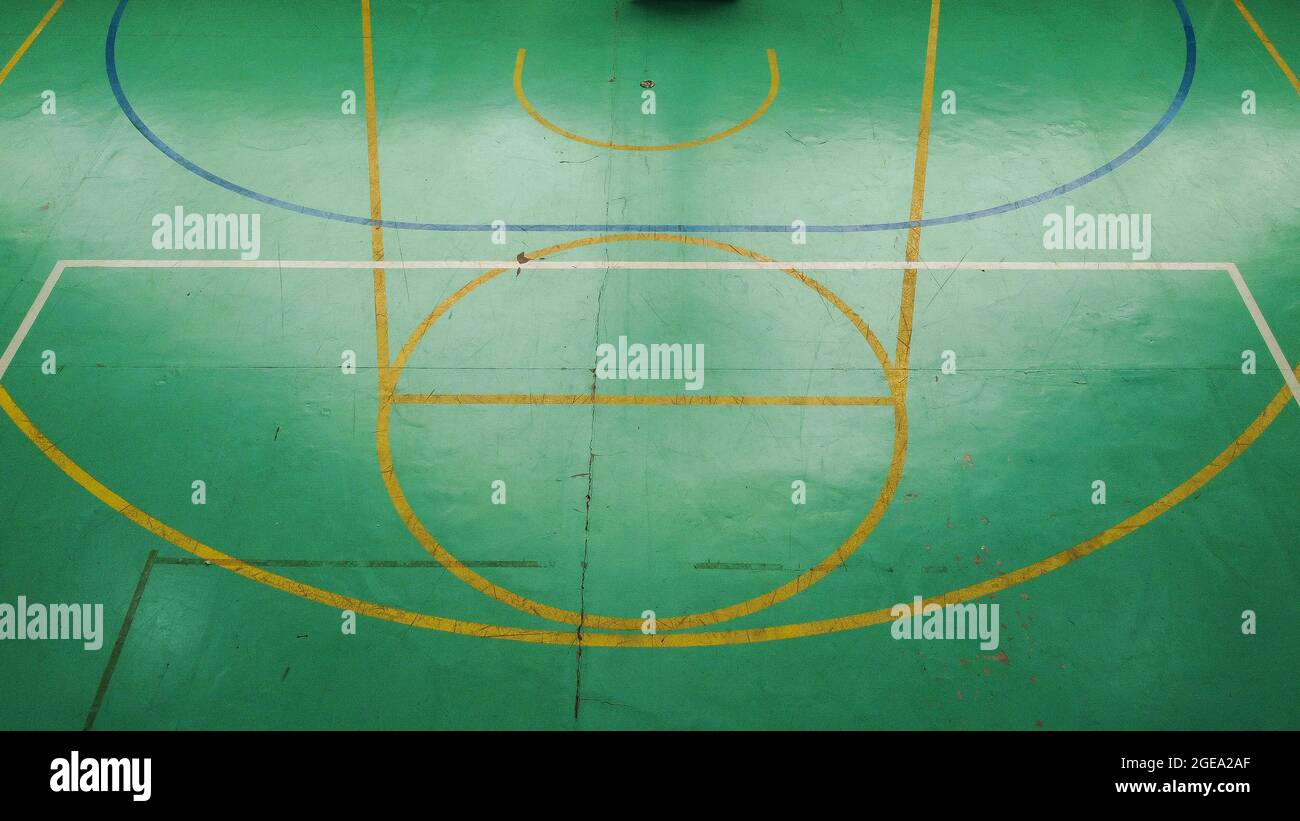 Green basketball court seen from above, with various marks of time, its