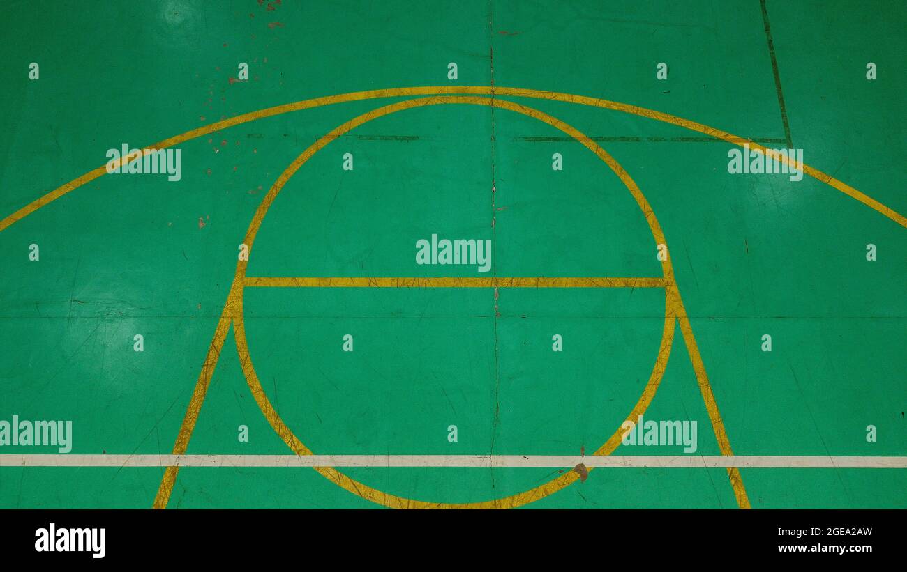 Green basketball court seen from above, with various marks of time, its