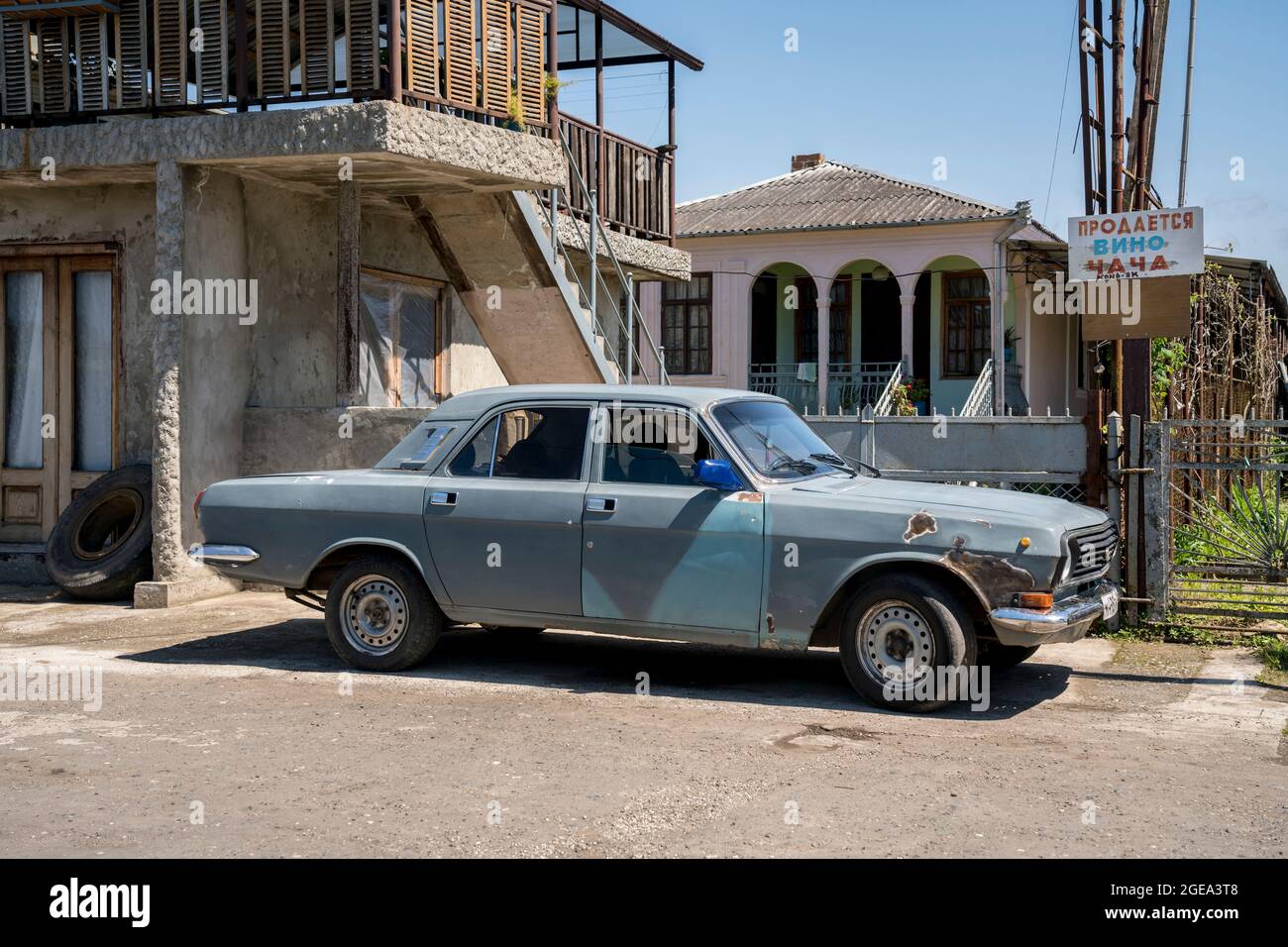 A Soviet car next to an advertisement for chacha which is a local wine product in the war ravaged seaside town of Ochamchire in Abkhazia. Stock Photo