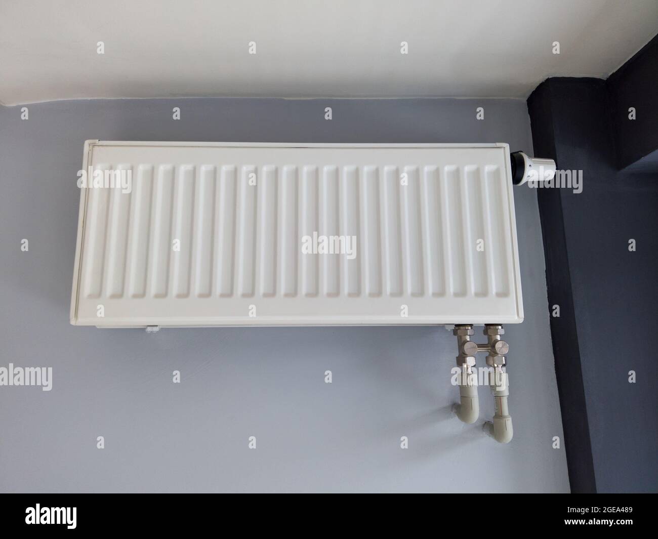 White heating radiator with thermostat on gray wall. Modern plastic